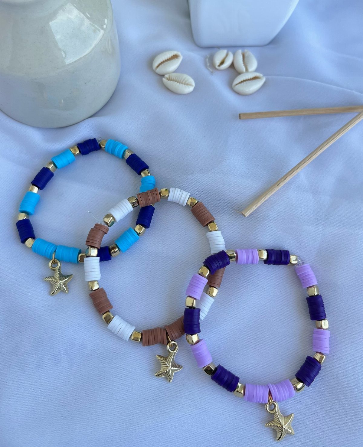 11 Beaded Jewelry DIY Bracelets Ideas for Every Style 1 Three colorful clay bead bracelets with gold star charms on white fabric.