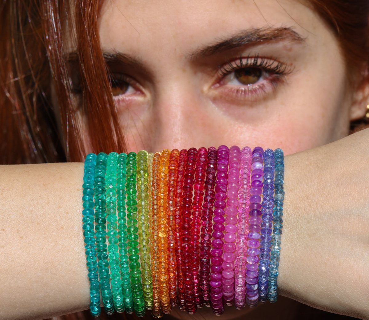 11 Beaded Jewelry DIY Bracelets Ideas for Every Style 10 Rainbow colored beaded bracelets stacked on a wrist in front of a face.