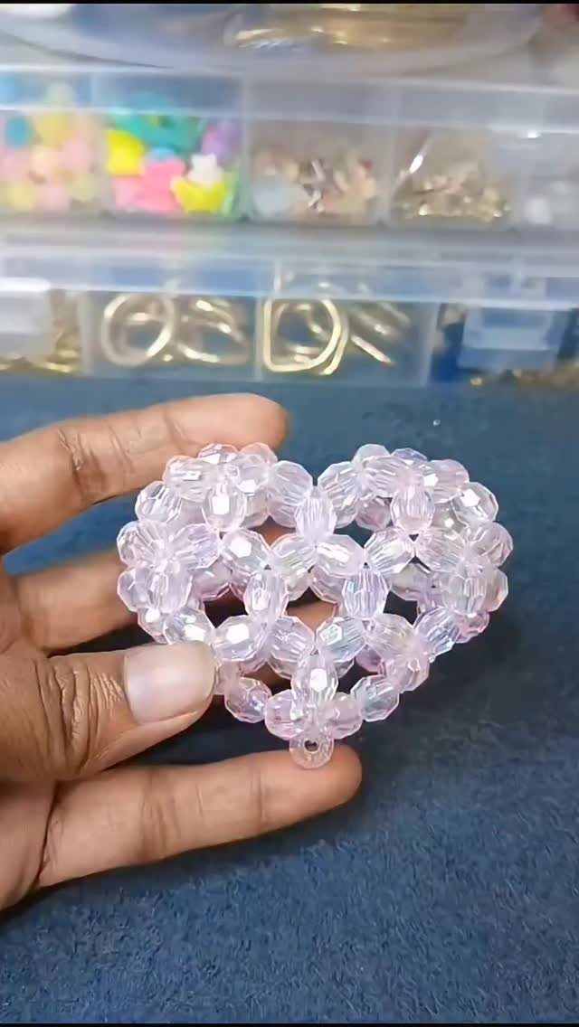Three-dimensional heart made of translucent pink beads held in a person's hand.