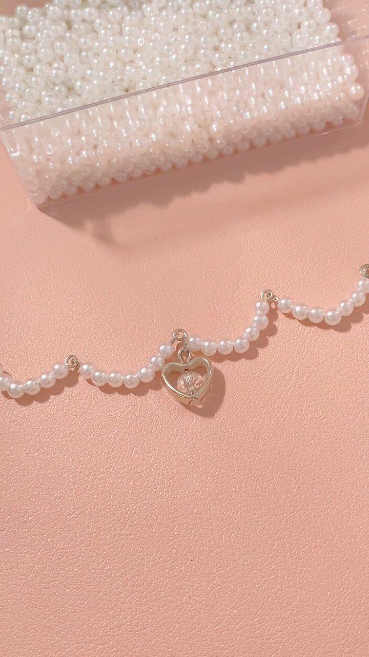 White beaded bracelet with a silver heart charm on a pink background