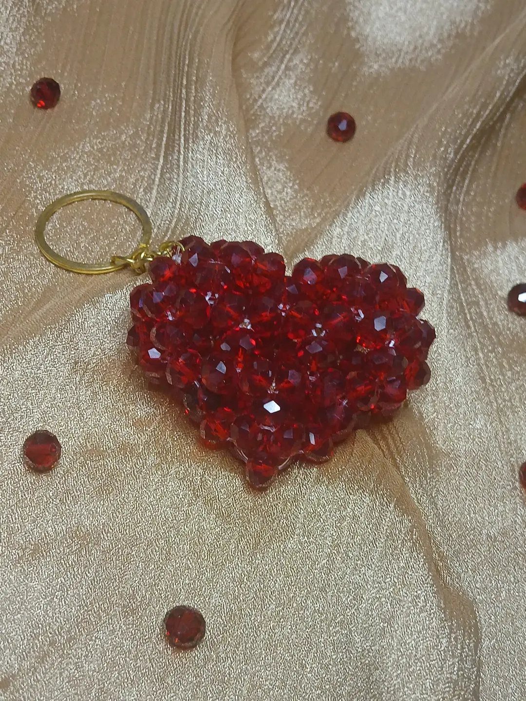 Red beaded heart keychain resting on shimmering gold fabric with loose red beads.