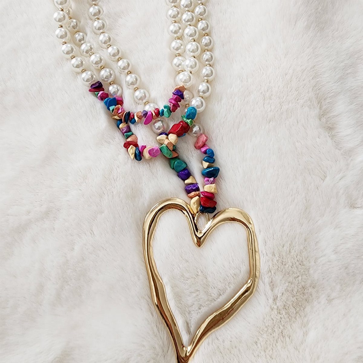 Gold heart pendant necklace with white pearls and colorful beads on white fur.