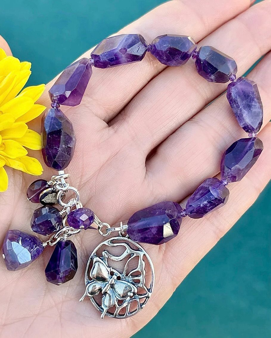 Purple amethyst beaded bracelet with a silver butterfly charm held in a hand.