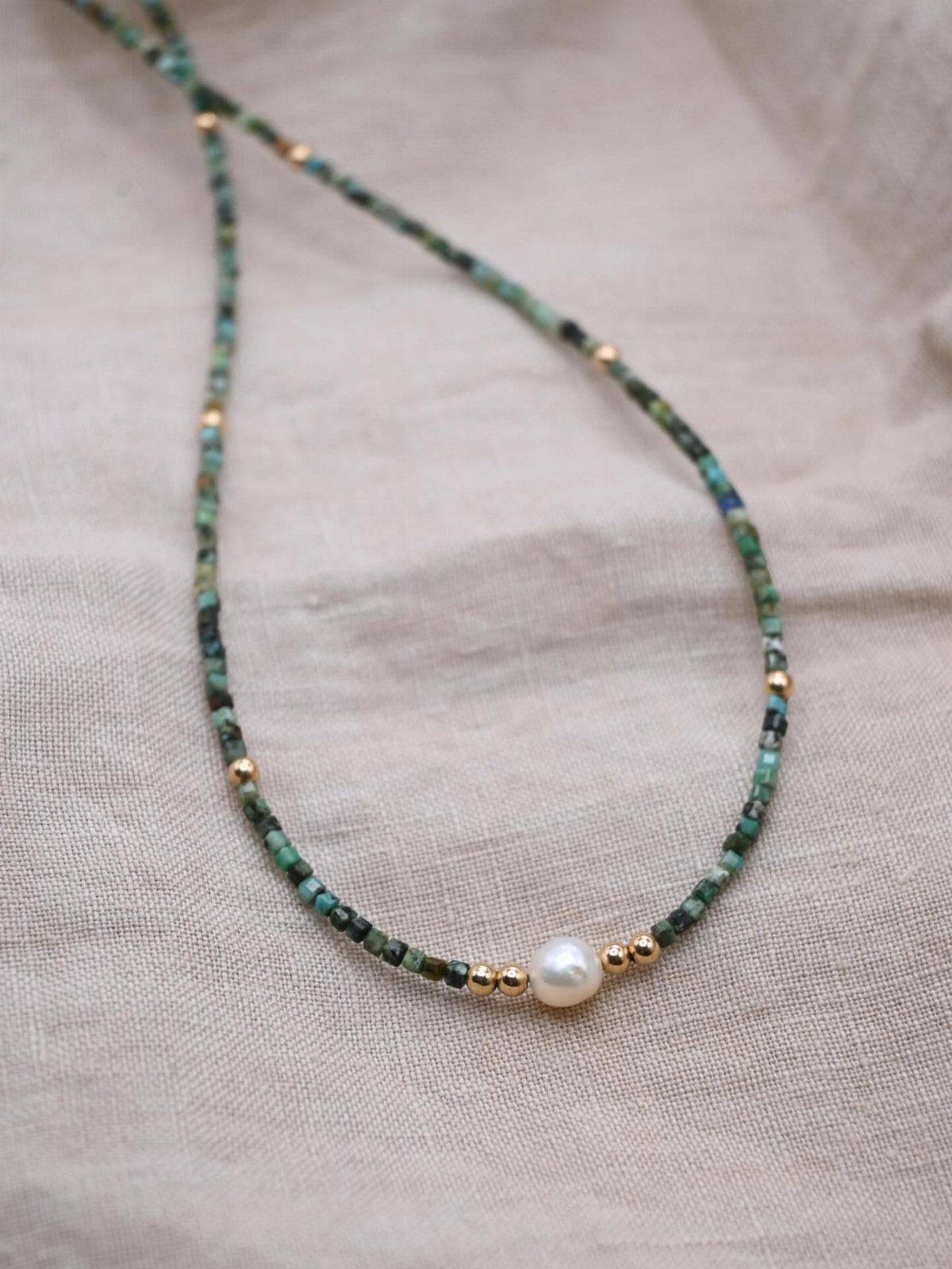 Beaded necklace with green beads and a central pearl on beige linen