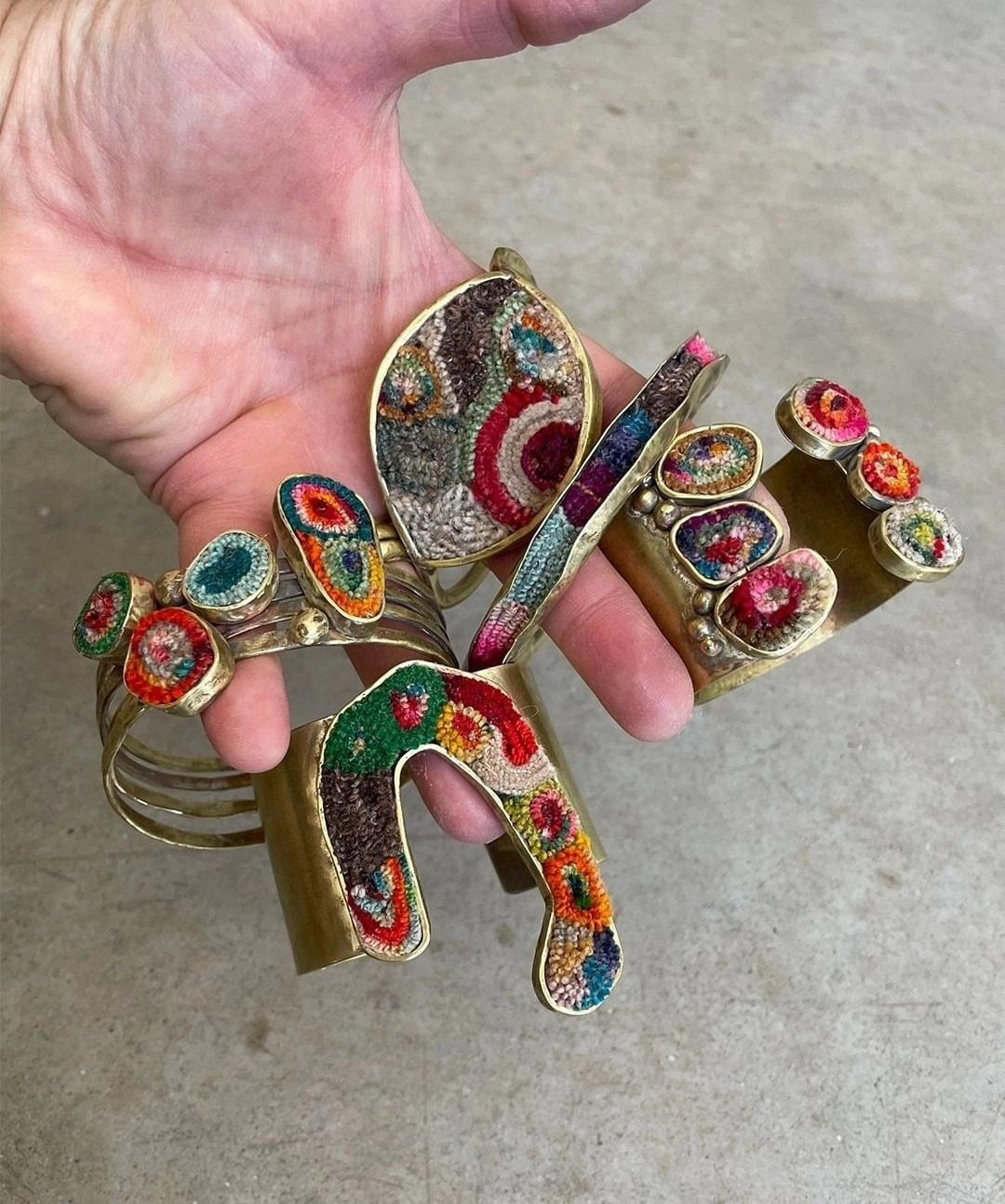 Gold metal bracelets with colorful beaded inlays held in a person's hand.