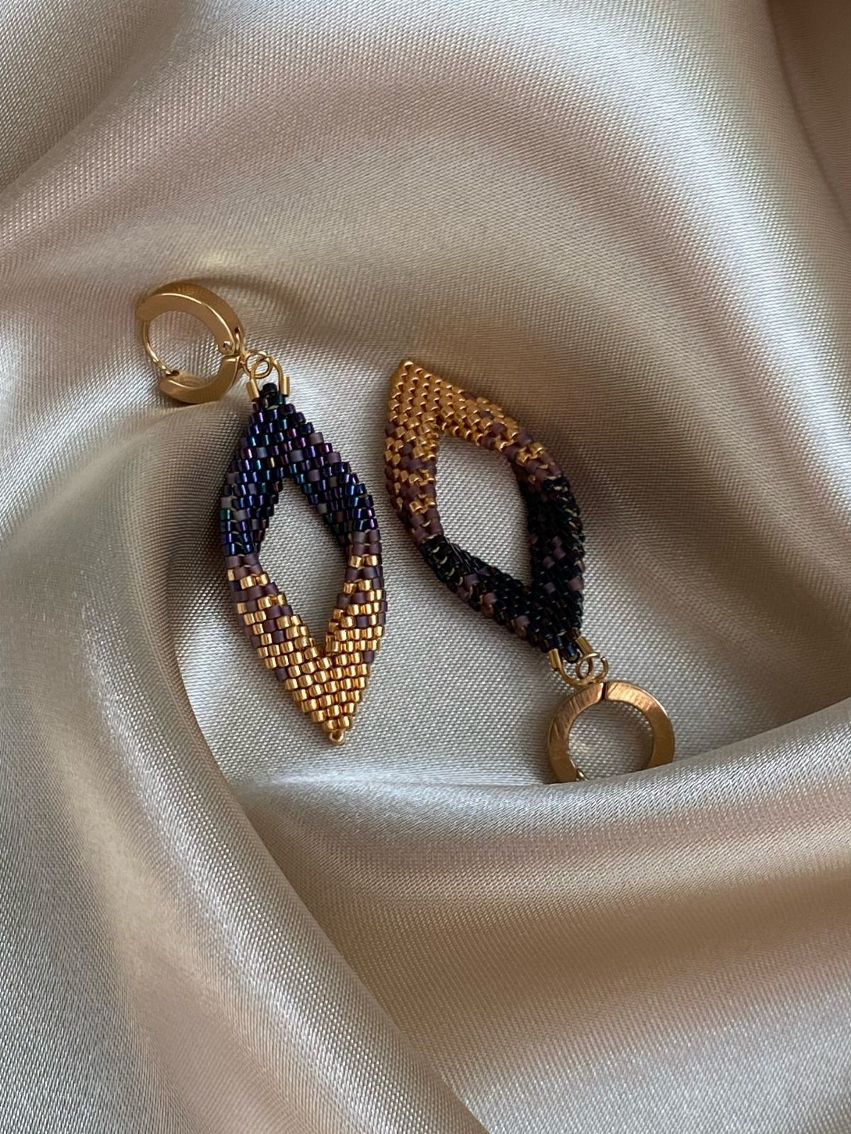 16 Beaded Jewelry Ideas to DIY (Bracelets, Necklaces & Earrings) 10 Diamond-shaped beaded earrings with gold, purple, and blue beads on satin fabric.