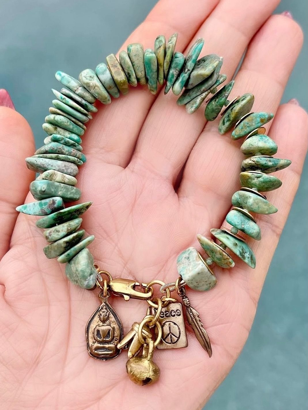 16 Beaded Jewelry Ideas to DIY (Bracelets, Necklaces & Earrings) 9 Turquoise stone chip bracelet with Buddha and peace sign charms held in a hand