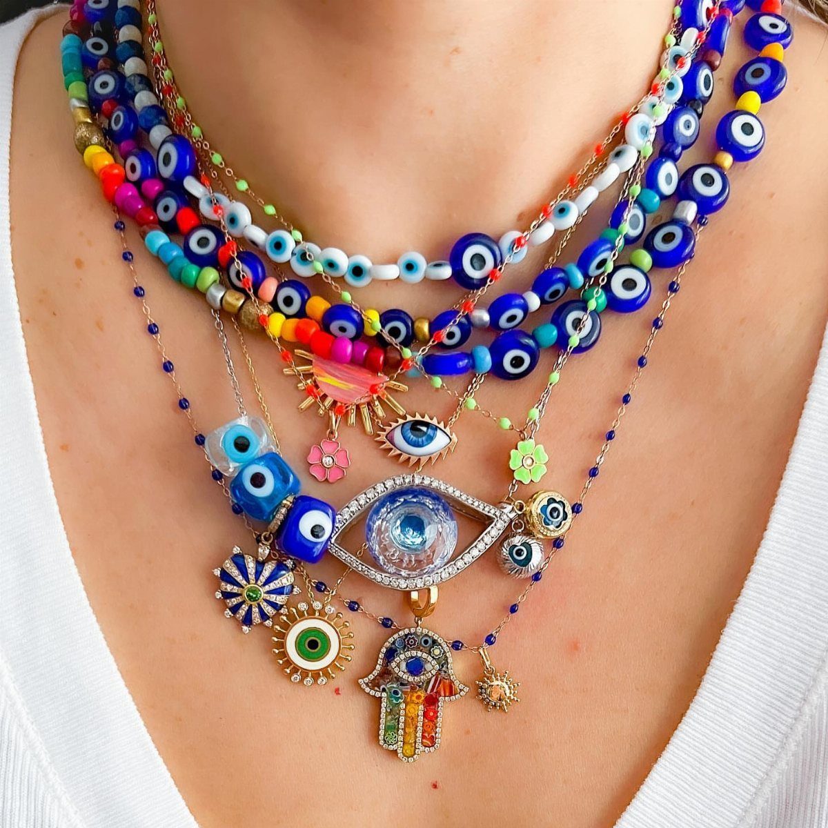 16 Beaded Jewelry Ideas to DIY (Bracelets, Necklaces & Earrings) 6 Stacked beaded necklaces with blue evil eye charms and a Hamsa hand pendant.