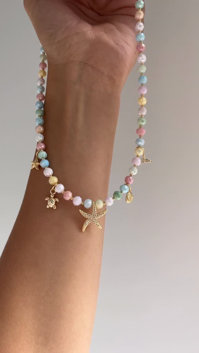 16 Beaded Jewelry Ideas to DIY (Bracelets, Necklaces & Earrings) 13 Pastel beaded necklace with gold starfish and turtle charms held by a hand.