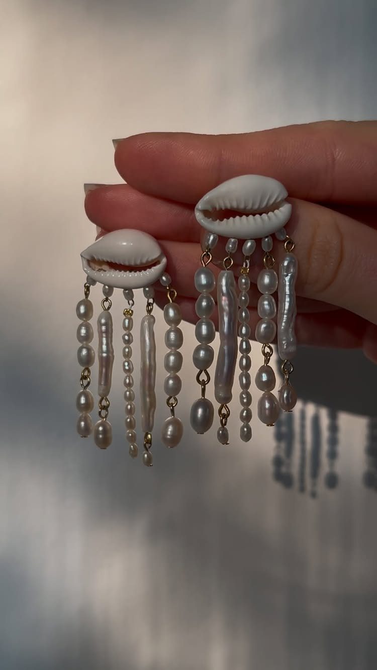 16 Beaded Jewelry Ideas to DIY (Bracelets, Necklaces & Earrings) 11 Handmade earrings with white cowrie shells and dangling white pearl strands held by hand.