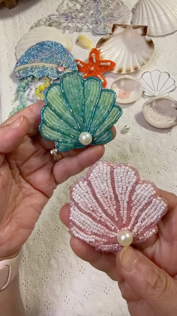 Beaded shell jewelry in green and pink held by hands among seashells