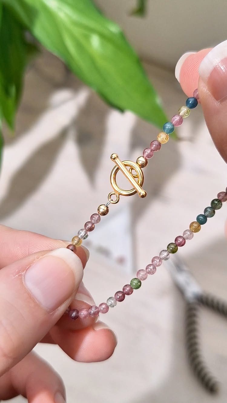 Beaded bracelet with multi-colored translucent beads and a gold toggle clasp held by hands.