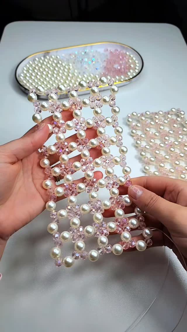 Hands holding a woven jewelry band made of white pearls and pink beads.