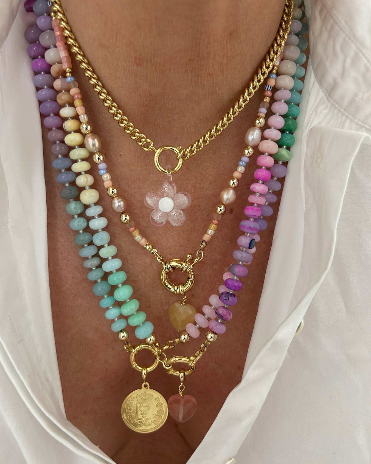 Beaded Jewelry Trends 2026: 8 Styles From Chunky Necklaces to Charm Accents 4 Layered beaded necklaces in pastel colors and gold chains worn on a person.