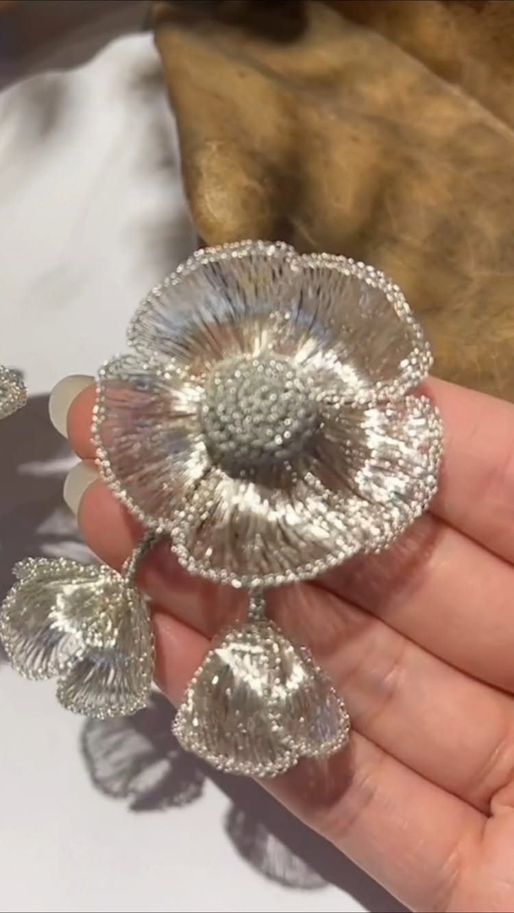 Beaded Jewelry Trends 2026: 8 Styles From Chunky Necklaces to Charm Accents 5 Silver beaded sculptural jewelry shaped like a flower held in a hand.