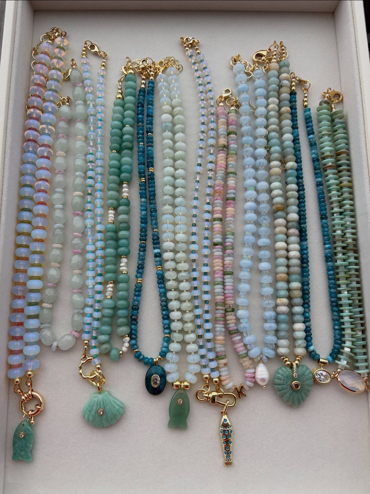 Beaded Jewelry Trends 2026: 8 Styles From Chunky Necklaces to Charm Accents 8 Assorted blue and pastel beaded necklaces with shell charms on a white background