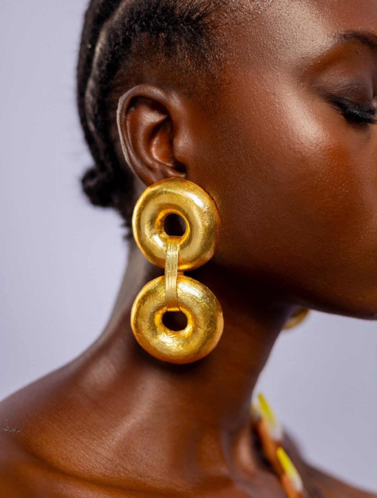 Bold Gold Jewelry: 9 Ways to Wear the Trend in 2026 8 Large textured gold hoop earrings worn by a person with dark skin.