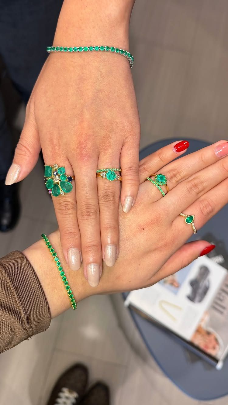 Bold Gold Jewelry: 9 Ways to Wear the Trend in 2026 3 Hands wearing gold rings and bracelets featuring vibrant green gemstones.