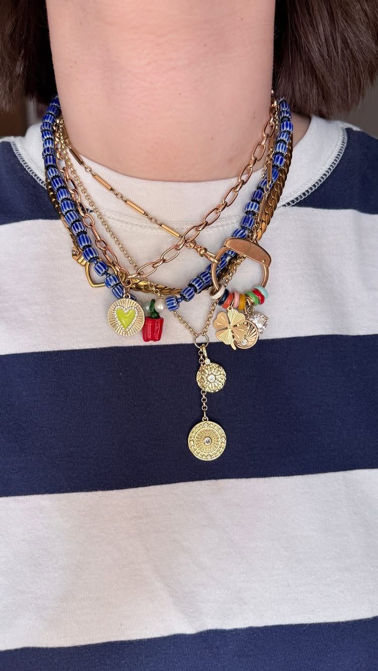 Bold Gold Jewelry: 9 Ways to Wear the Trend in 2026 4 Layered gold chains and blue beaded necklaces with charms on a striped shirt