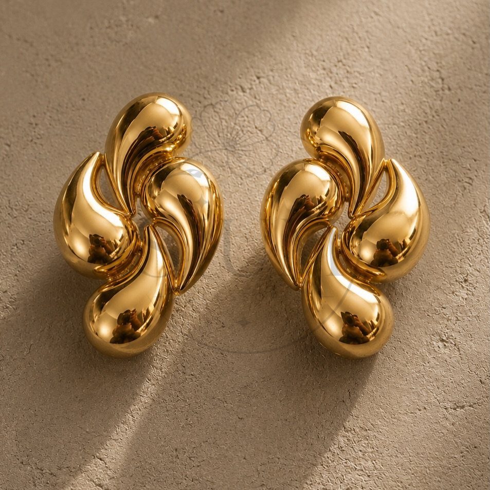 Bold Gold Jewelry: 9 Ways to Wear the Trend in 2026 7 Gold earrings with swirling organic shapes resting on a textured grey stone surface