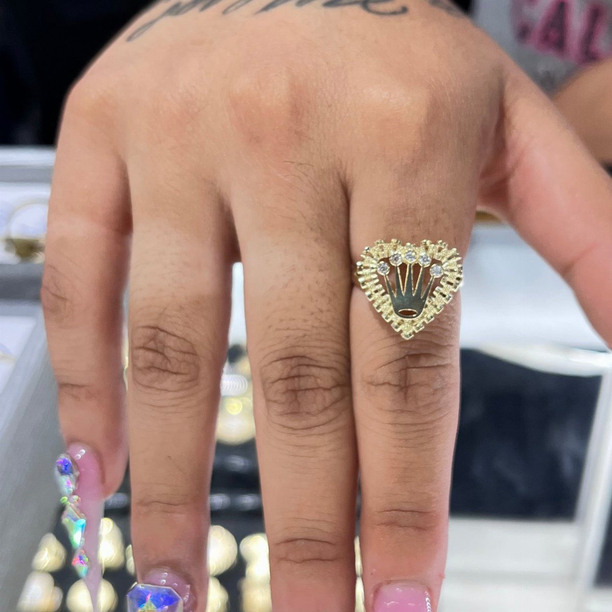6 Cali Gold Rings for Hearts, Chunky Bands and Twisted Styles 1 Gold heart-shaped ring with crystals worn on a finger with decorated nails