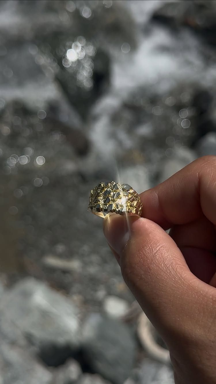 6 Cali Gold Rings for Hearts, Chunky Bands and Twisted Styles 3 Gold ring with a rough textured surface held against a blurred rocky stream