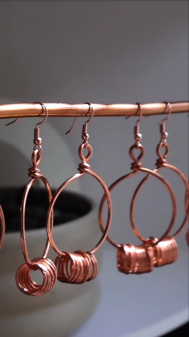 Copper wire hoop earrings with coiled accents hanging from a copper rod