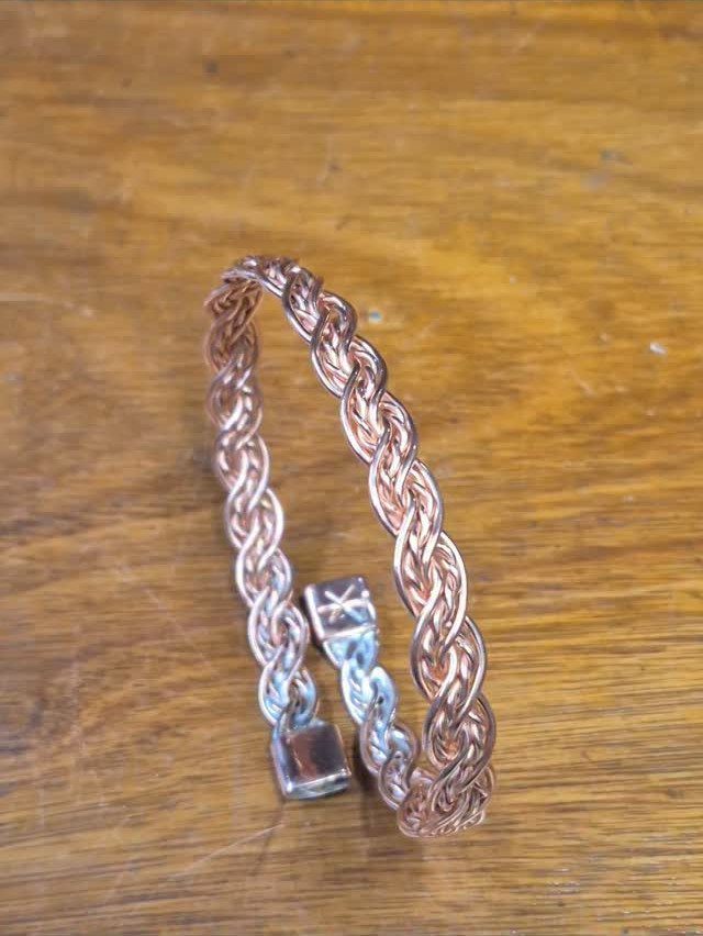 Braided copper wire bracelet with a clasp on a wooden background