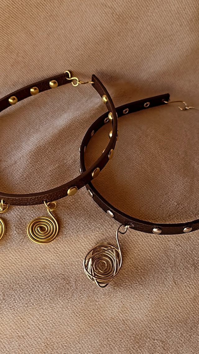Brown leather chokers with metal studs and copper wire spiral pendants on beige fabric