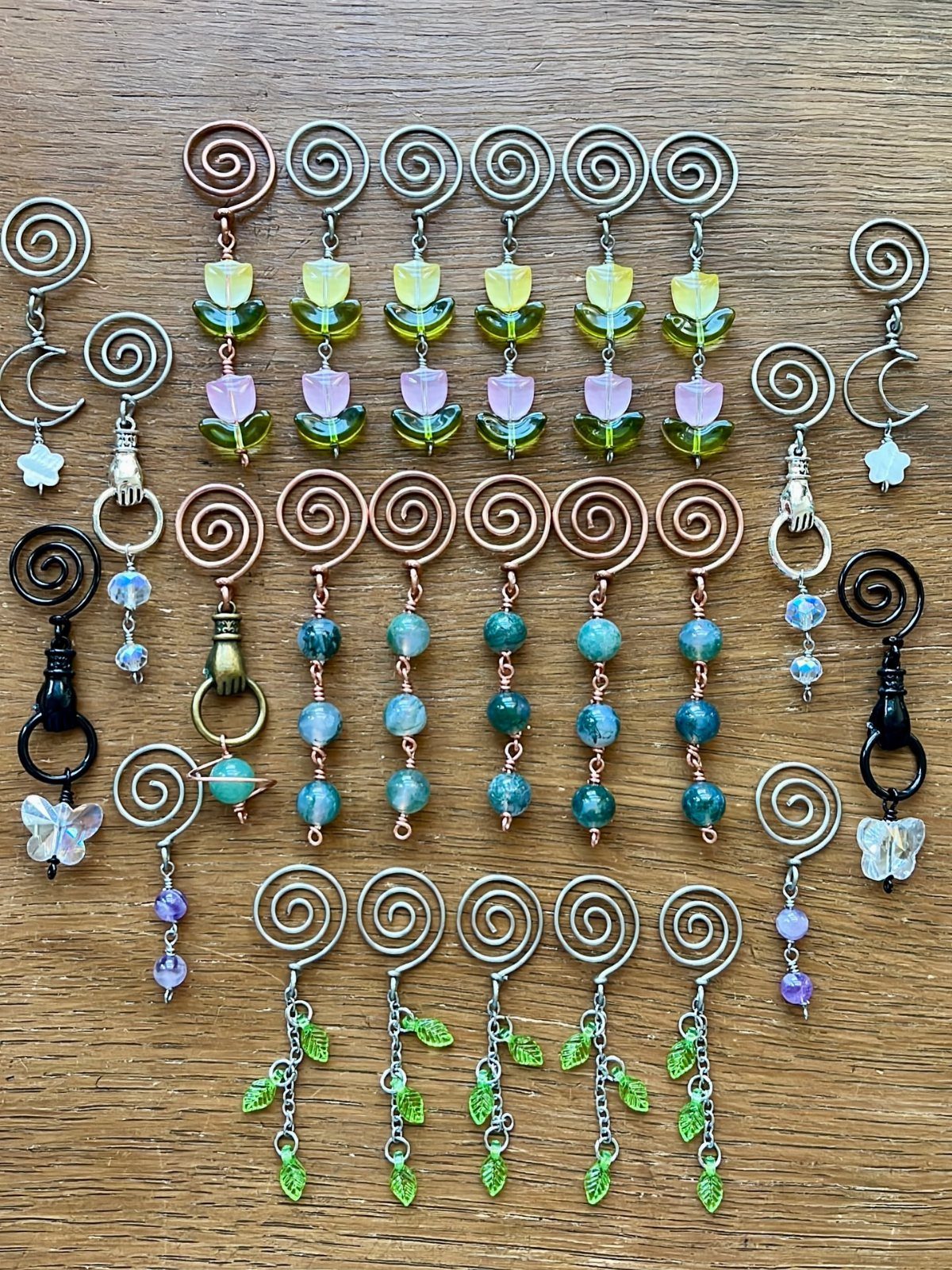 Copper wire jewelry with spirals, colorful beads, and green leaves on wood