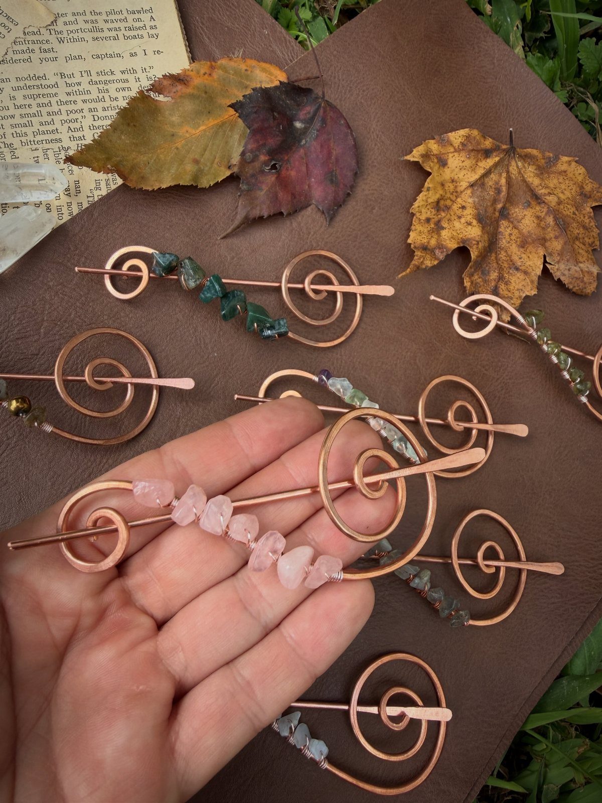 Copper wire hair pins with crystals resting on brown leather and autumn leaves