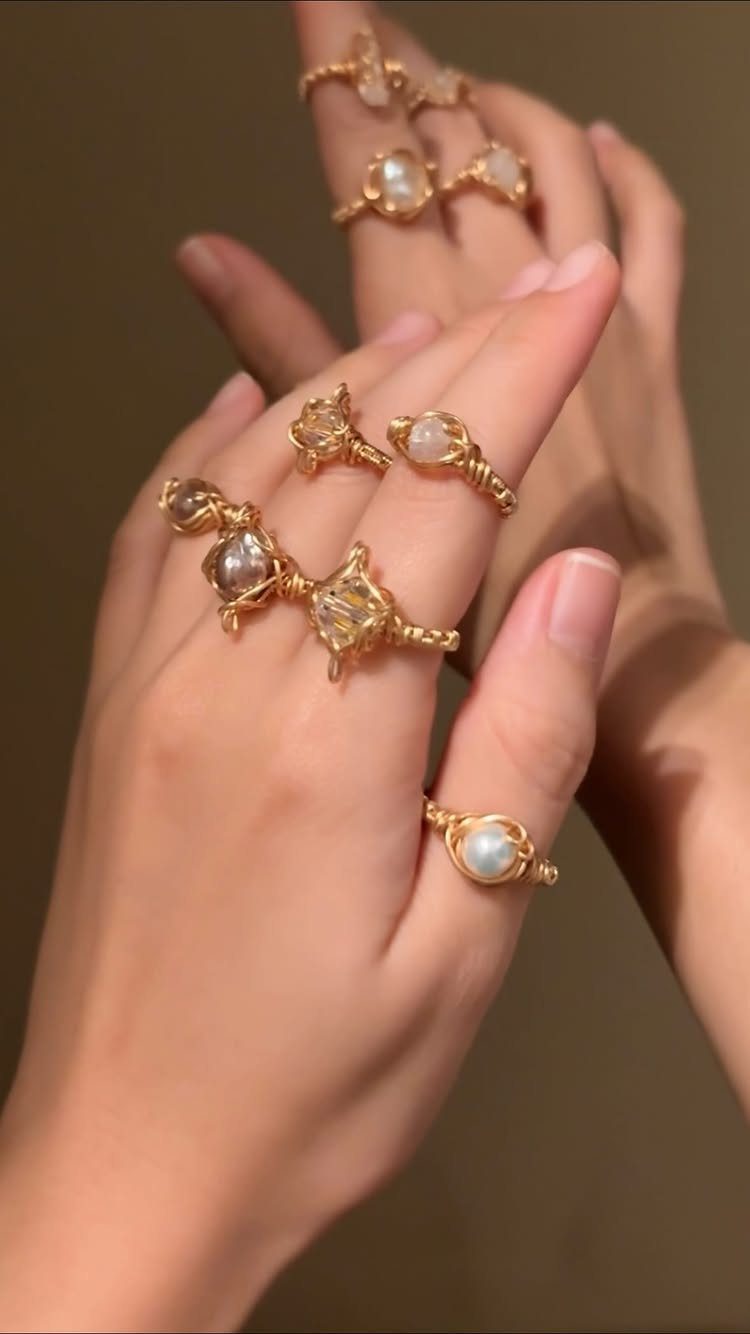 Gold wire-wrapped rings with gemstones worn on multiple fingers of a hand.