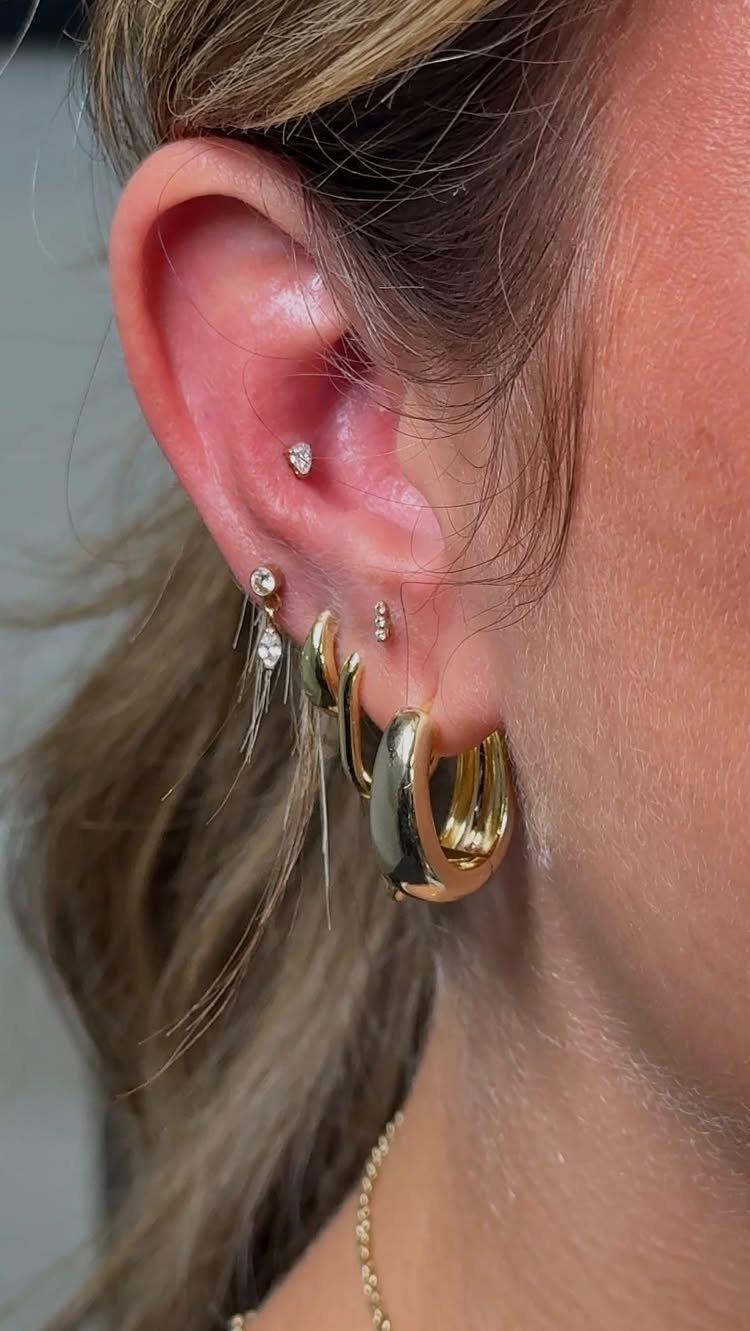 Ear with multiple gold piercings including a conch stud and lobe hoops.