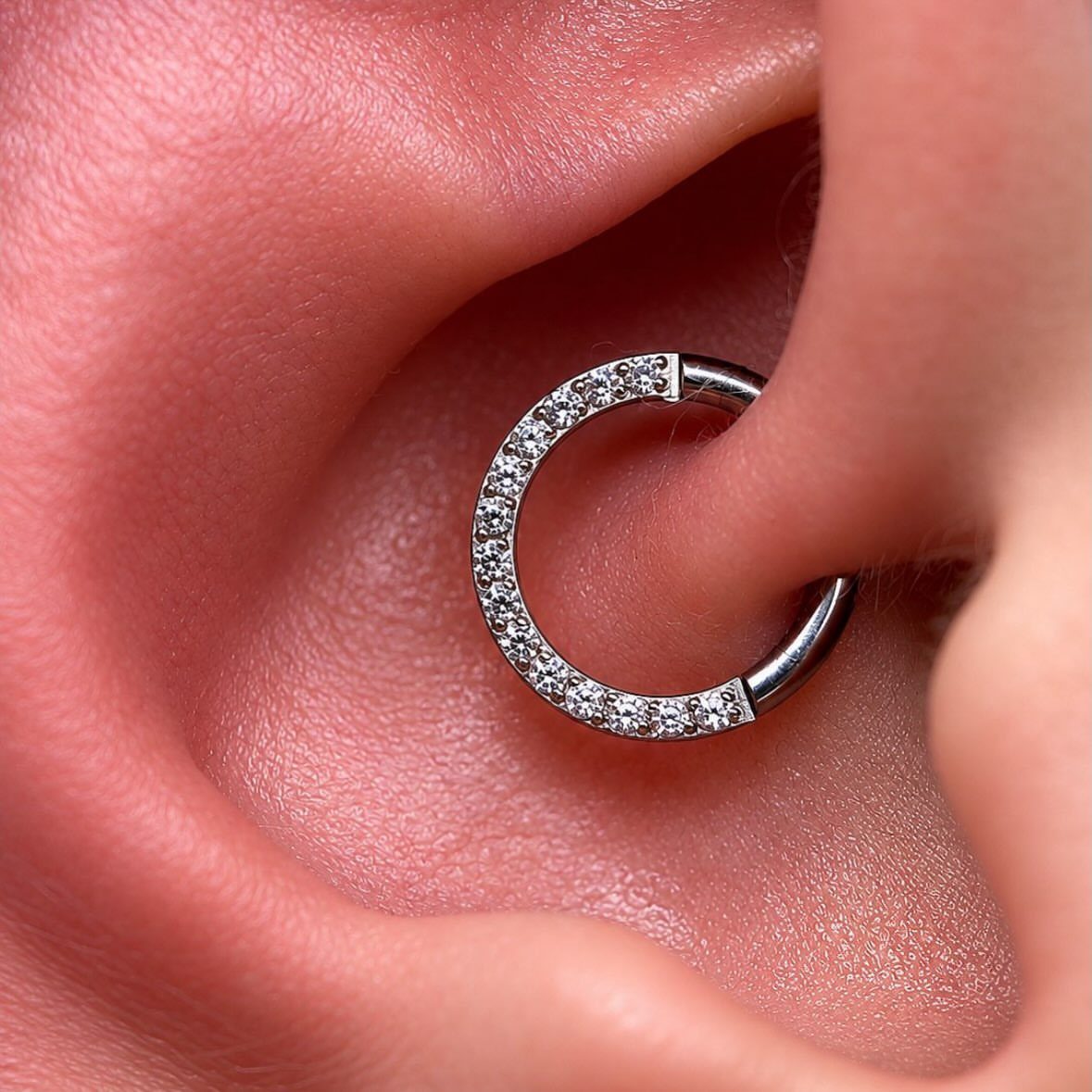 Silver crystal hoop piercing in the daith fold of a human ear.
