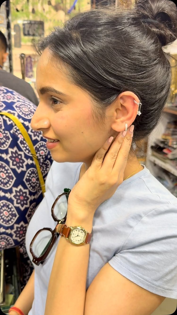 Woman with dark hair showing a helix hoop and lobe stud piercing.