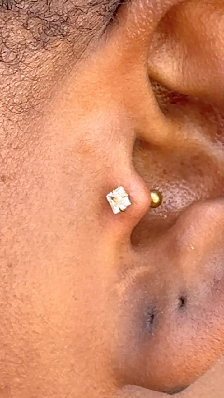 Ear with a sparkling stud in the tragus and a gold conch piercing.