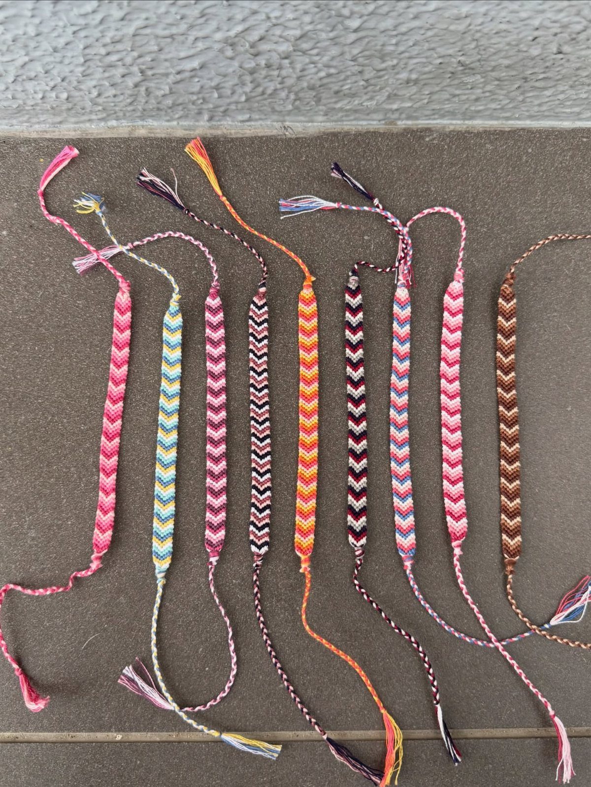 DIY Bracelet Designs: 8 Woven, Beaded and Leather Projects 4 Ten colorful woven friendship bracelets with chevron patterns on a grey stone surface.