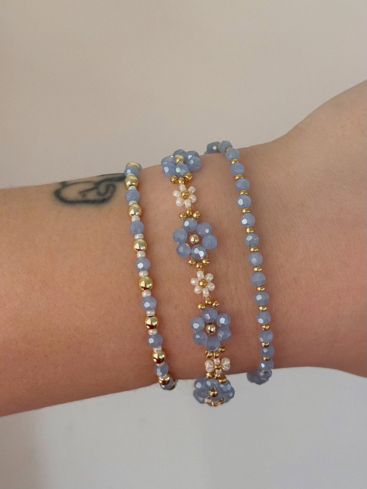 DIY Bracelet Designs: 8 Woven, Beaded and Leather Projects 5 Three blue and gold beaded bracelets, including one with floral patterns, on a wrist.