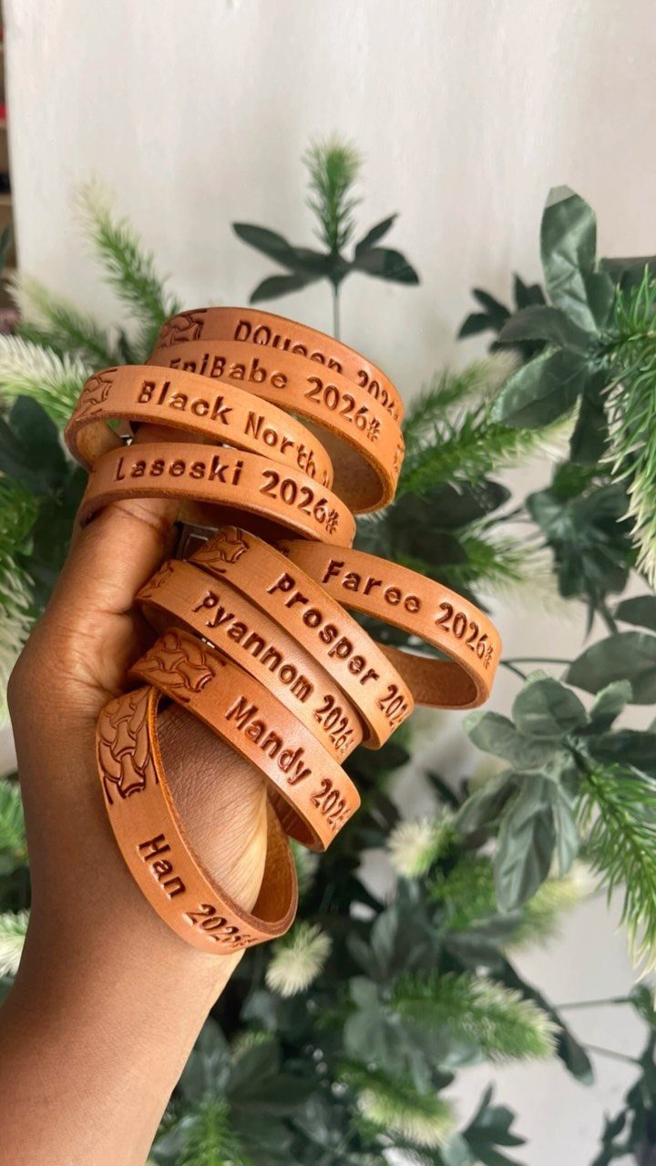 DIY Bracelet Designs: 8 Woven, Beaded and Leather Projects 2 Brown leather wrap bracelets with stamped names held against green foliage background