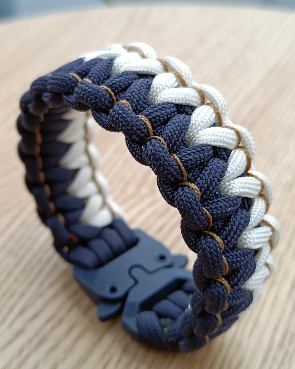 DIY Bracelet Designs: 8 Woven, Beaded and Leather Projects 3 Woven navy blue and white paracord survival bracelet with a black plastic buckle.