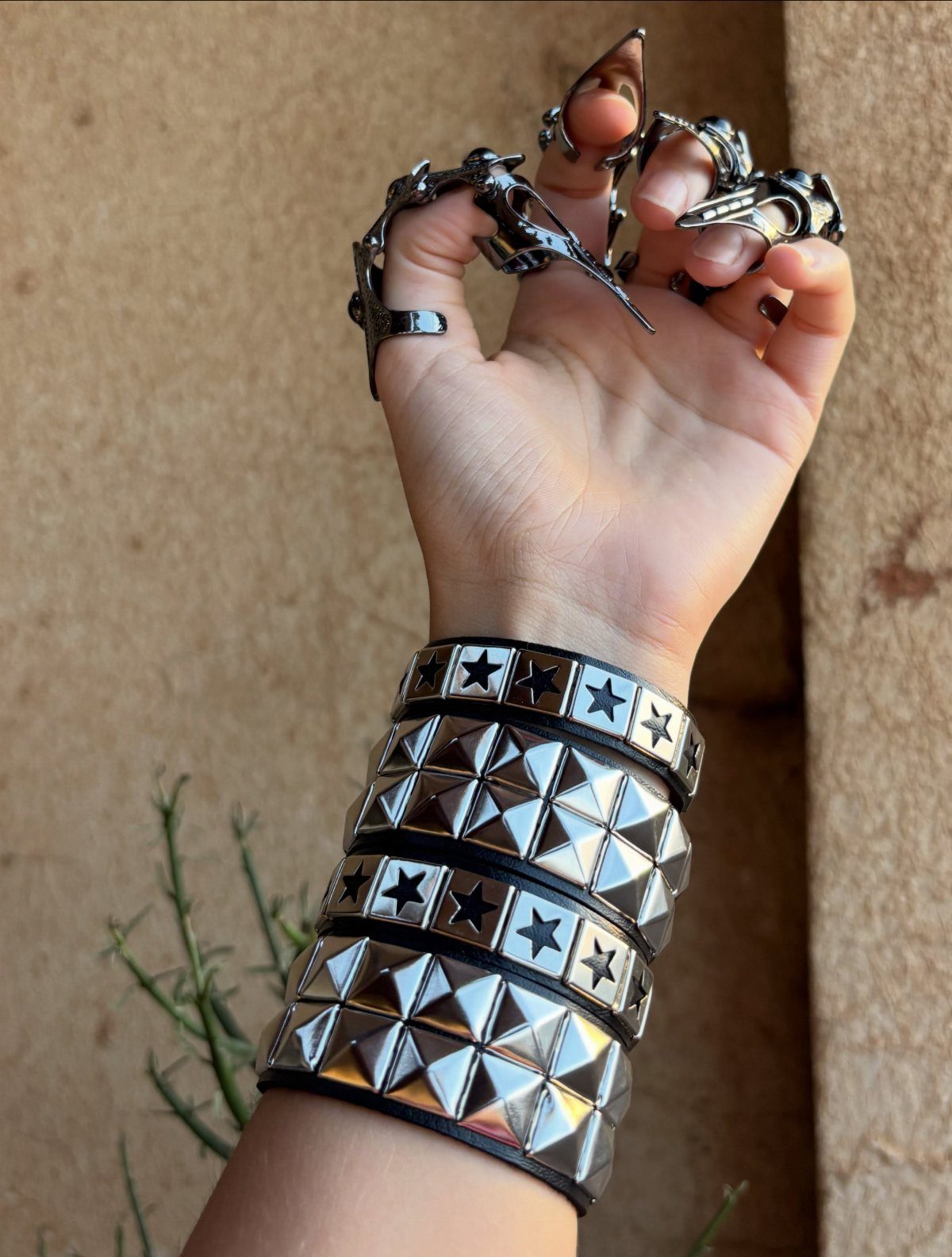 DIY Bracelet Designs: 8 Woven, Beaded and Leather Projects 8 Studded black leather bracelets and silver claw rings on a person's hand and wrist.