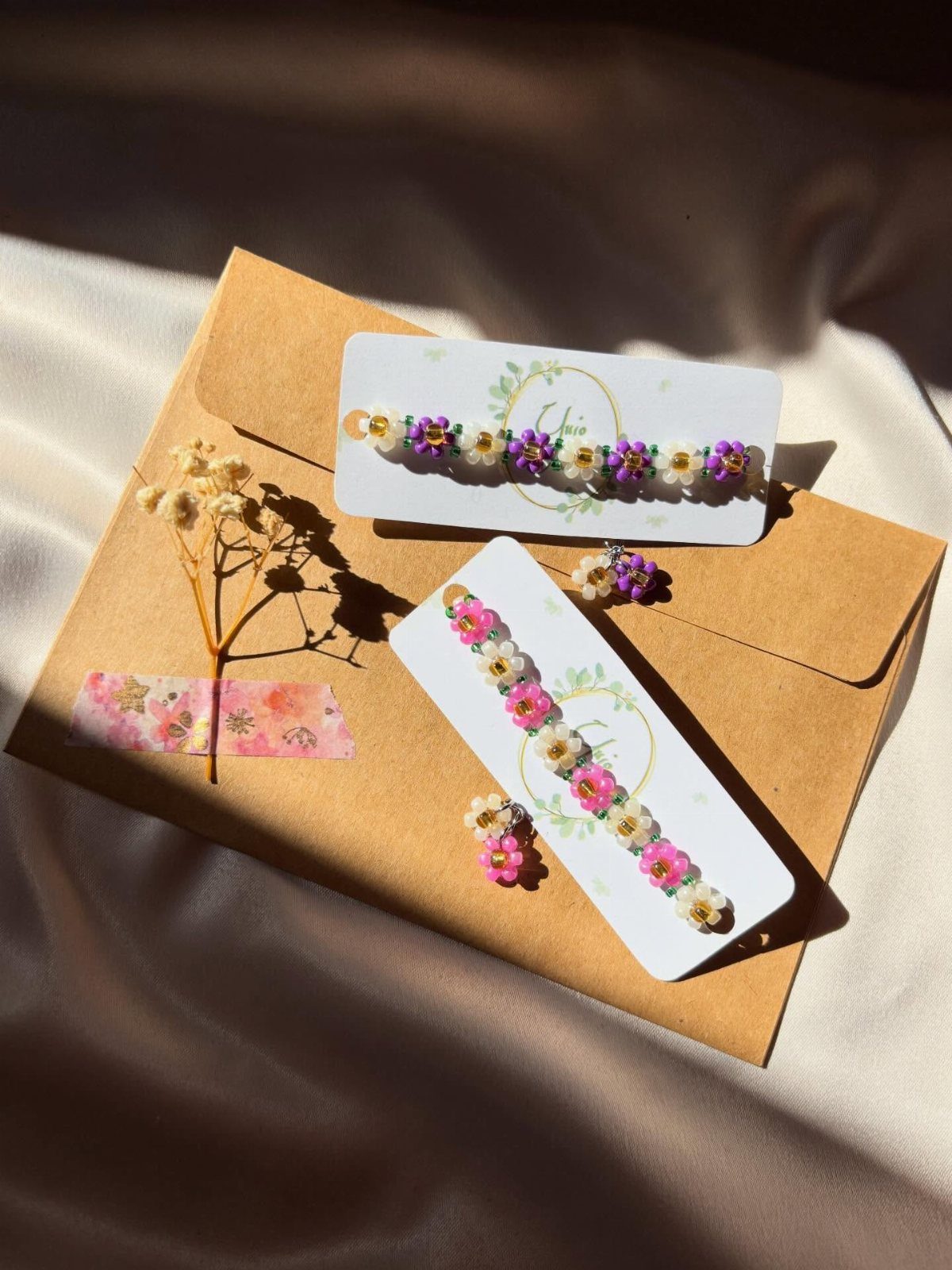 5 DIY Bracelets: Easy Beads Projects With Stretchy, Multi-Strand & More 5 Beaded flower bracelets on white cards resting on a brown envelope with dried flowers.