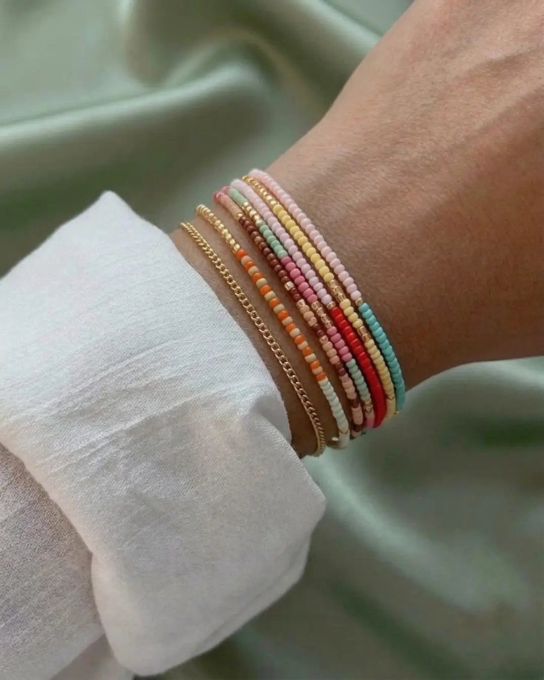 5 DIY Bracelets: Easy Beads Projects With Stretchy, Multi-Strand & More 2 Layered beaded bracelets in pastel colors and gold chain on a wrist