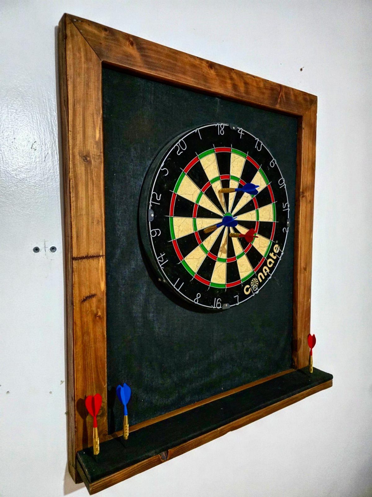 DIY Dart Board Backboard: 7 Clever Projects for Any Style 4 Dartboard mounted on a black fabric backboard with a wooden frame and shelf.