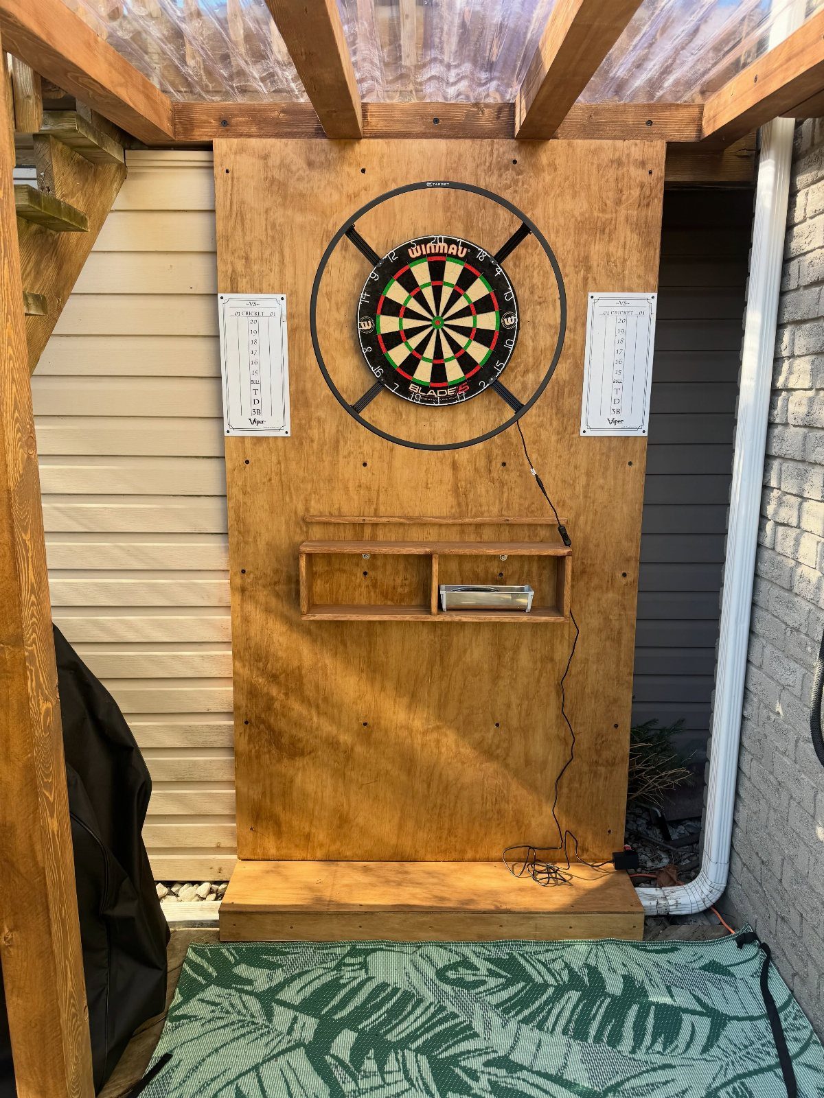 DIY Dart Board Backboard: 7 Clever Projects for Any Style 7 Dartboard mounted on a large plywood backboard with a small wooden shelf below.