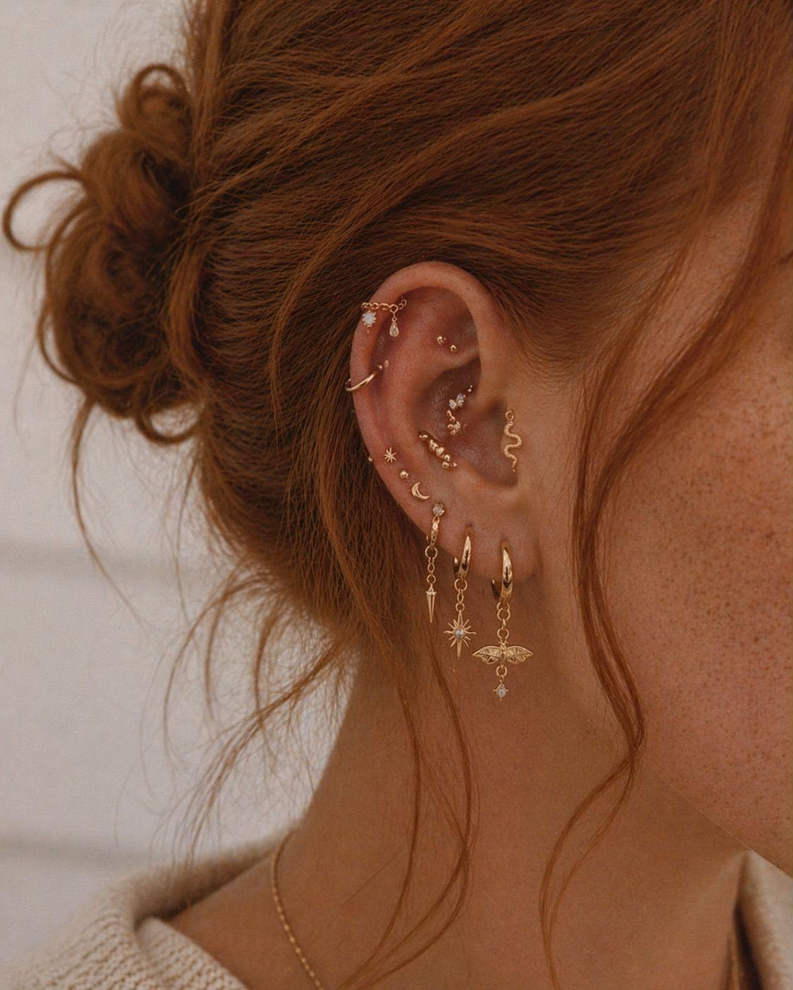 11 Ear Piercing Stack Inspo Ideas to Upgrade Your Look 2 Ear with multiple gold piercings featuring star and moon charms in a constellation pattern.