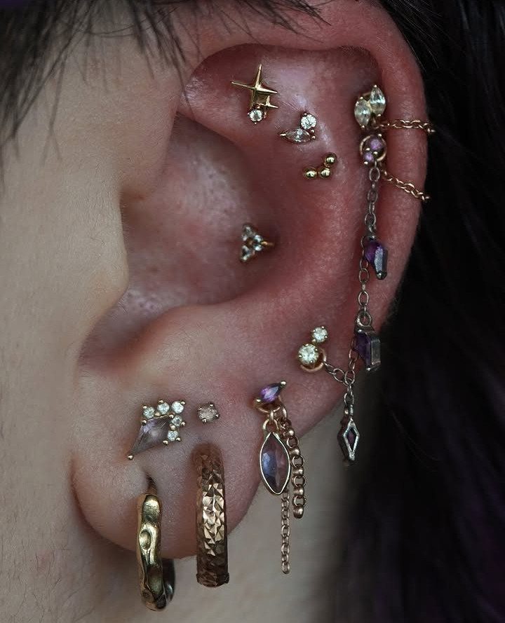 11 Ear Piercing Stack Inspo Ideas to Upgrade Your Look 4 Ear with a curated stack of gold jewelry, purple gemstones, and connecting chains.