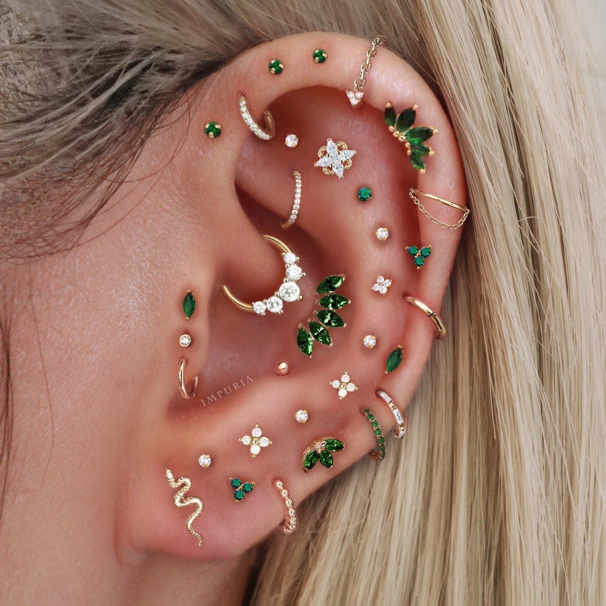 11 Ear Piercing Stack Inspo Ideas to Upgrade Your Look 9 Ear with multiple gold piercings featuring green gemstones and clear crystal studs.