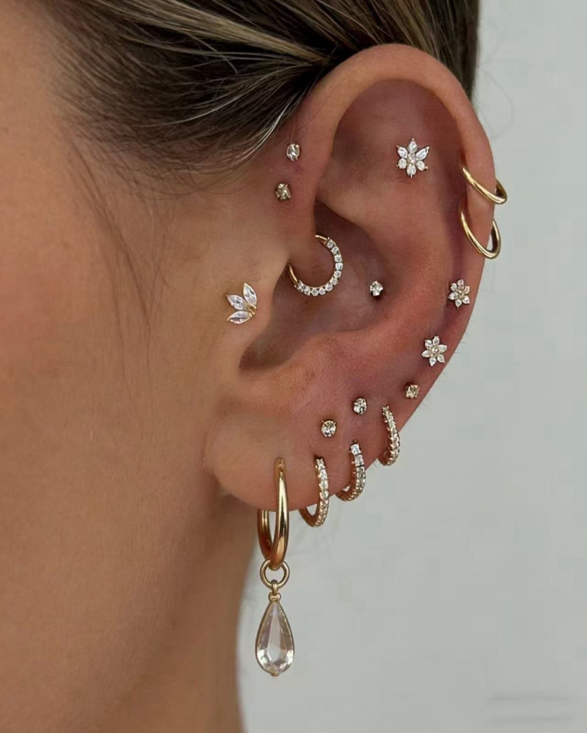11 Ear Piercing Stack Inspo Ideas to Upgrade Your Look 1 Ear with multiple gold piercings featuring a mix of studs and hoop earrings.