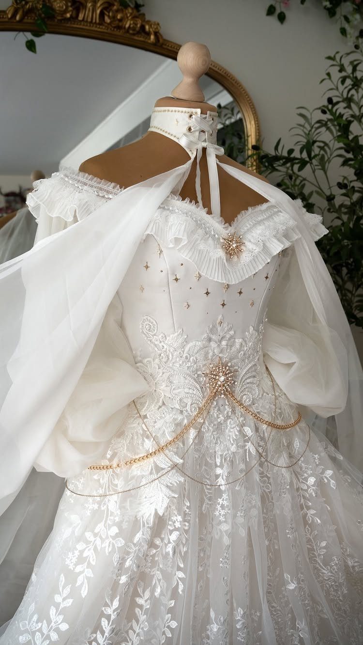 Ornate white fantasy wedding gown with lace, gold chains, and a sheer cape.